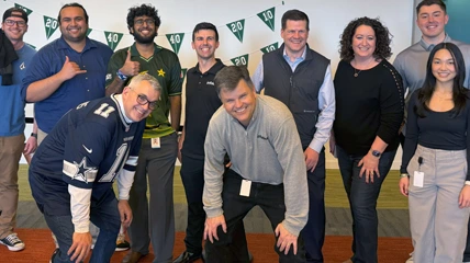 Groupe de collègues souriant et posant ensemble lors d'un événement à thème avec des décorations de drapeaux verts.