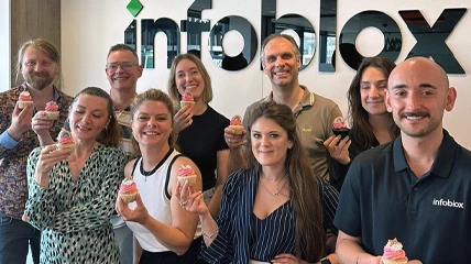 Groupe de collègues souriant et tenant des cupcakes devant le logo Infoblox.